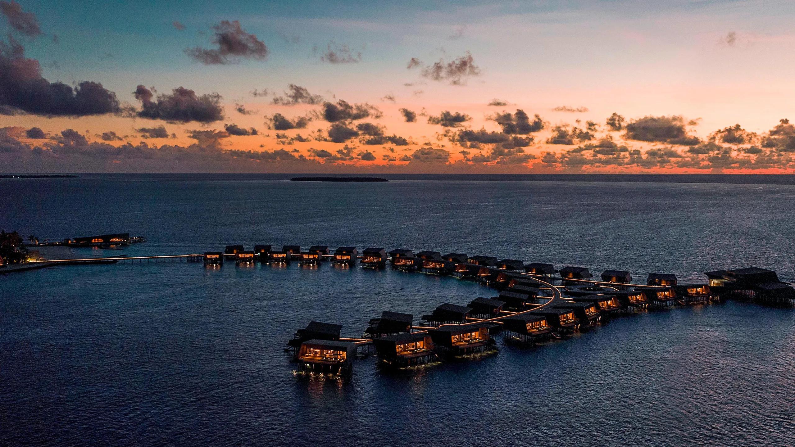 The resort's overwater villas lit at evening, seen from the air