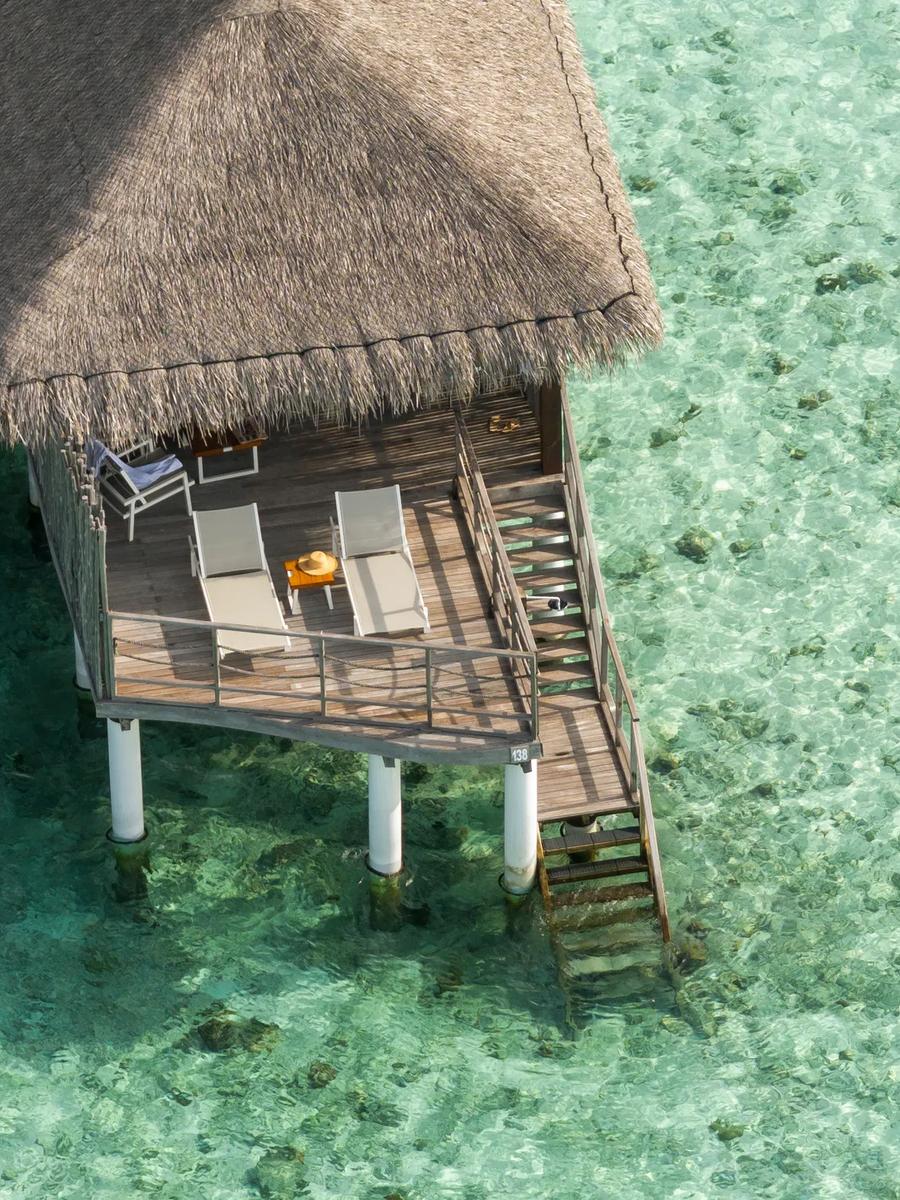 Aerial view of a single Water Villa's thatched roof and sun-deck standing on stilts over clear reef water