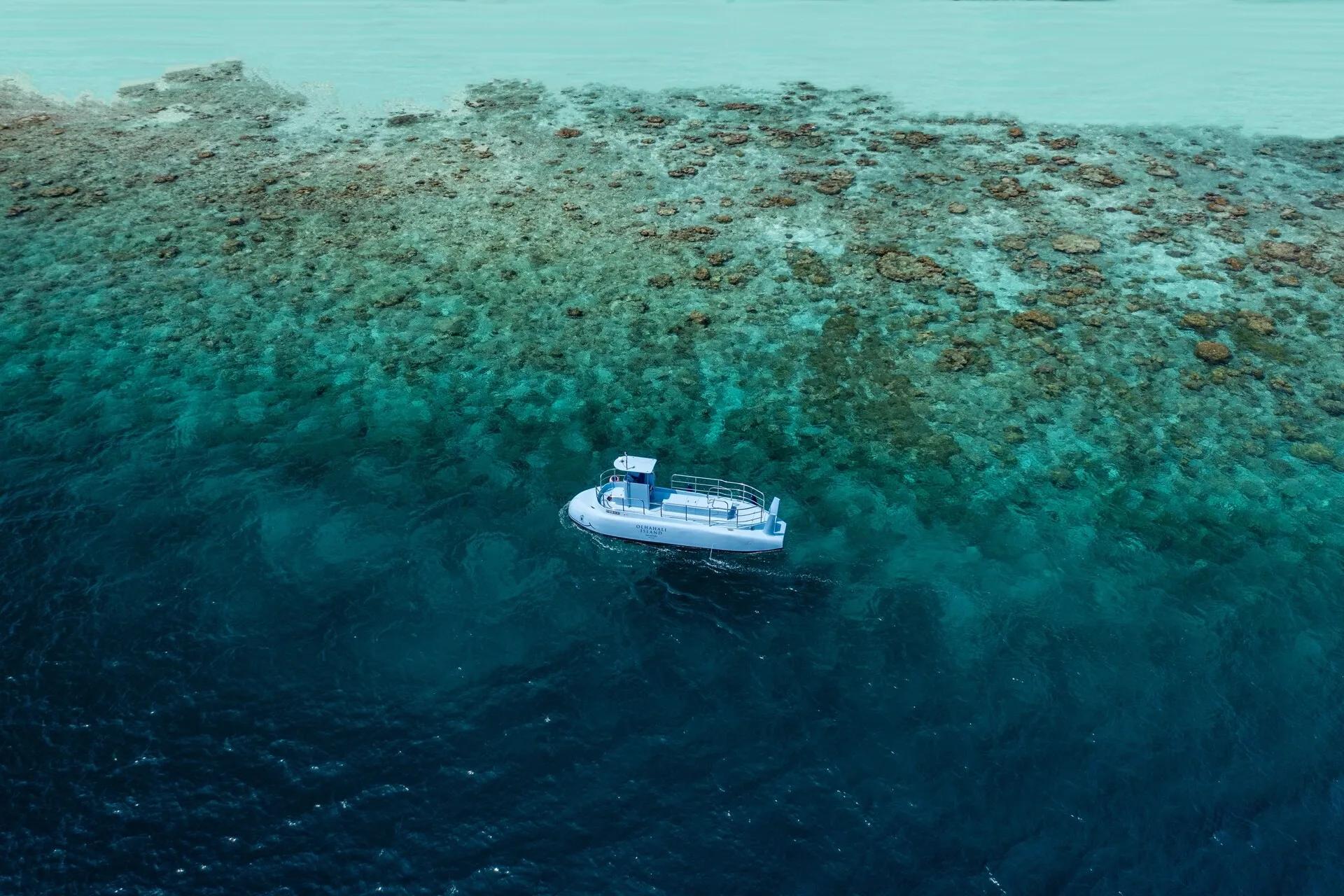 Jumeirah Olhahali's semi-submarine gliding over a coral reef, the water shifting from turquoise shallows to deep blue
