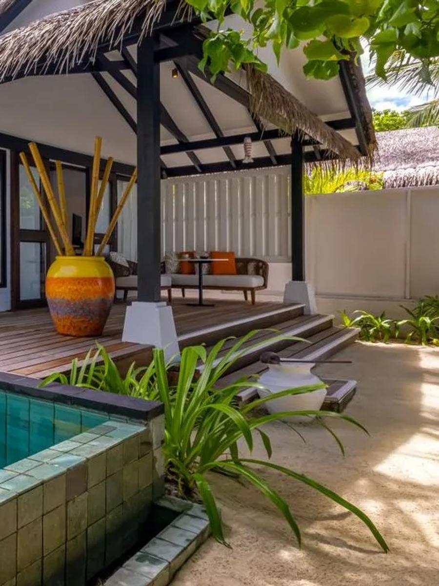 A beach villa's private pool bordered by dark tile, the thatched-roof villa and deck behind it