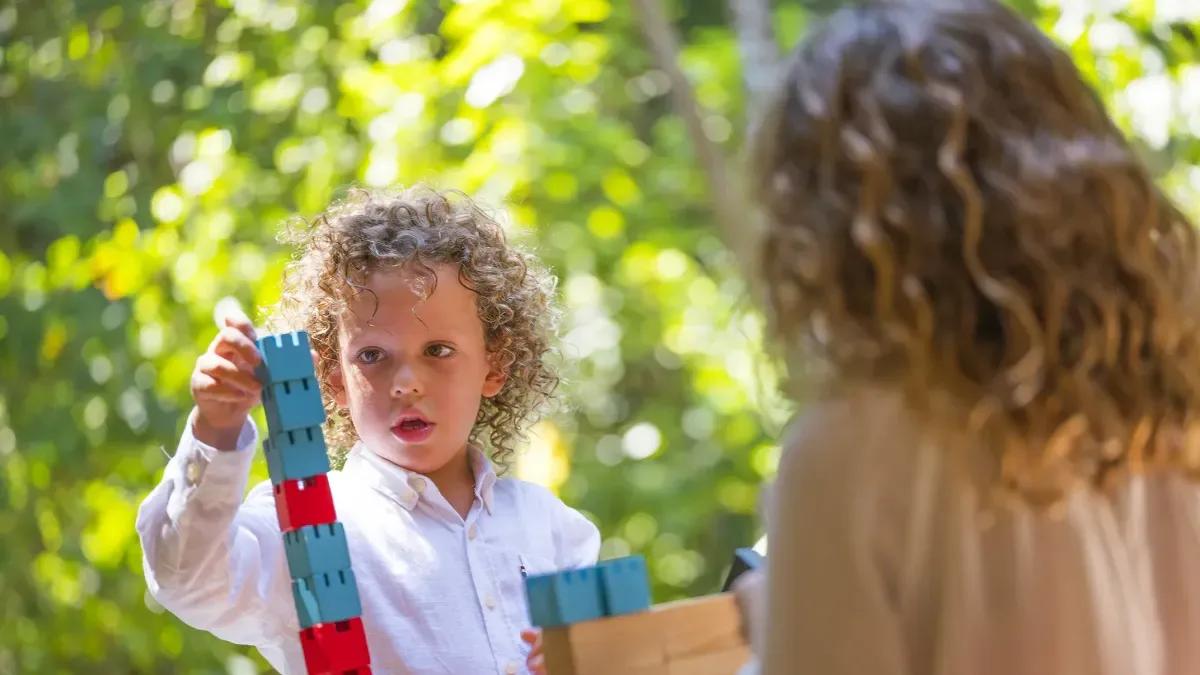 A young child stacking building blocks at Parrotfish Club, a parent looking on