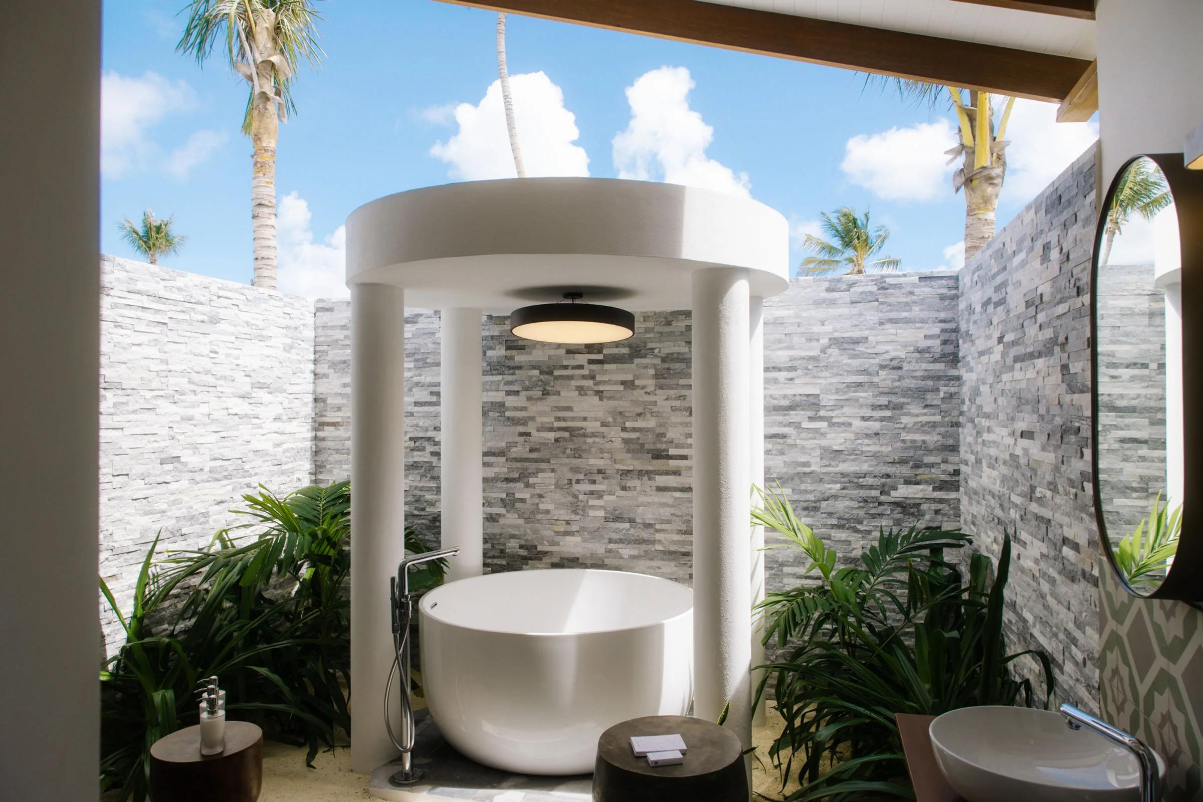The Beach Residence's outdoor bathing area, a round freestanding tub set beneath an open pavilion among palm trees