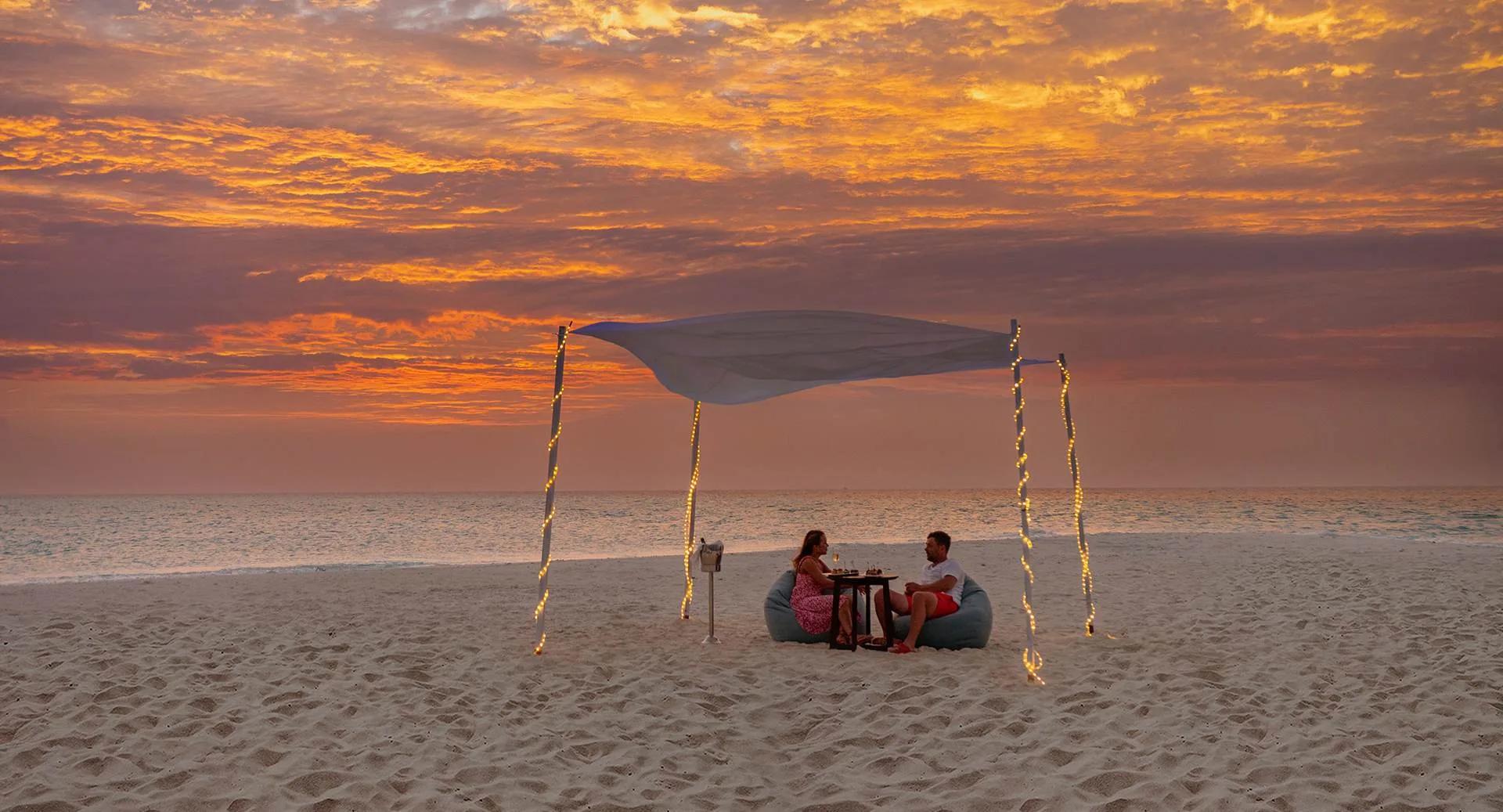 A private canopied dinner set on the beach at sunset at NH Maldives Kuda Rah