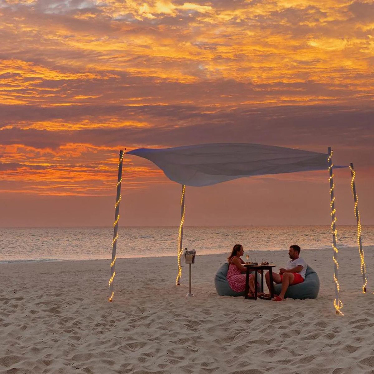 A private canopied dinner set on the beach at sunset at NH Maldives Kuda Rah