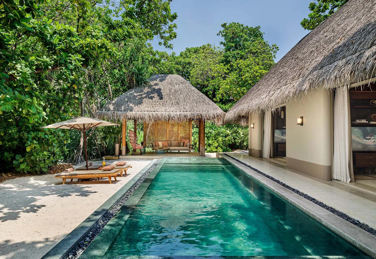 The long pool running alongside a Two Bedroom Beach Villa with Pool, with a second thatched pavilion and hanging chair in the garden