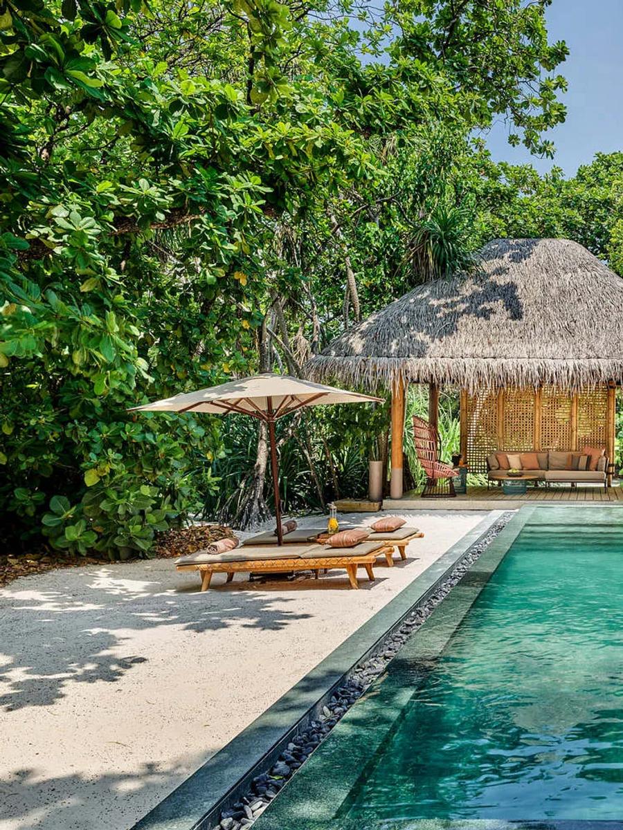 The long pool running alongside a Two Bedroom Beach Villa with Pool, with a second thatched pavilion and hanging chair in the garden