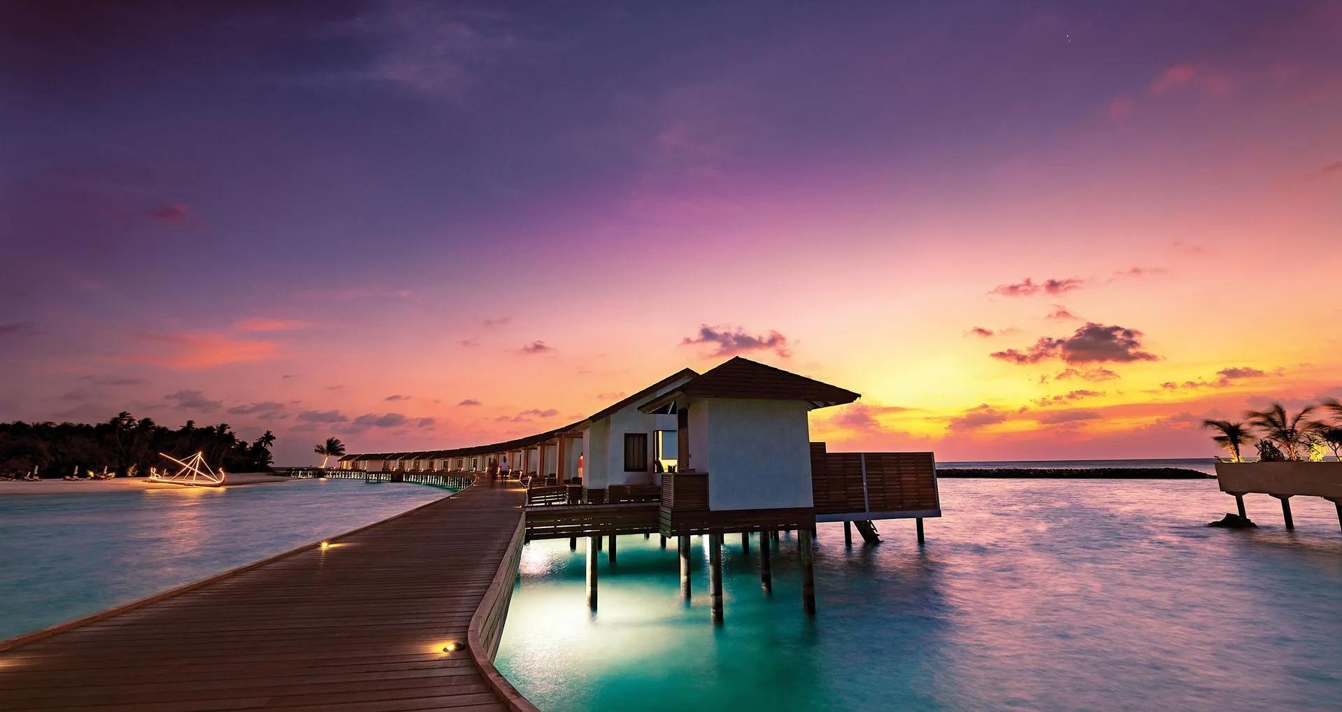The Water Villa row lit at sunset, connected by a boardwalk above the lagoon