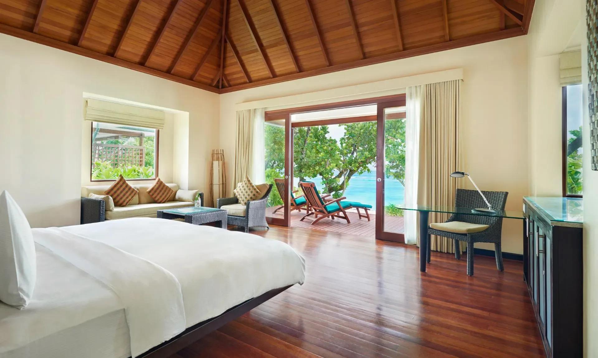 Beach Villa bedroom with a king bed facing a private deck and daybeds, the lagoon visible through the open doors
