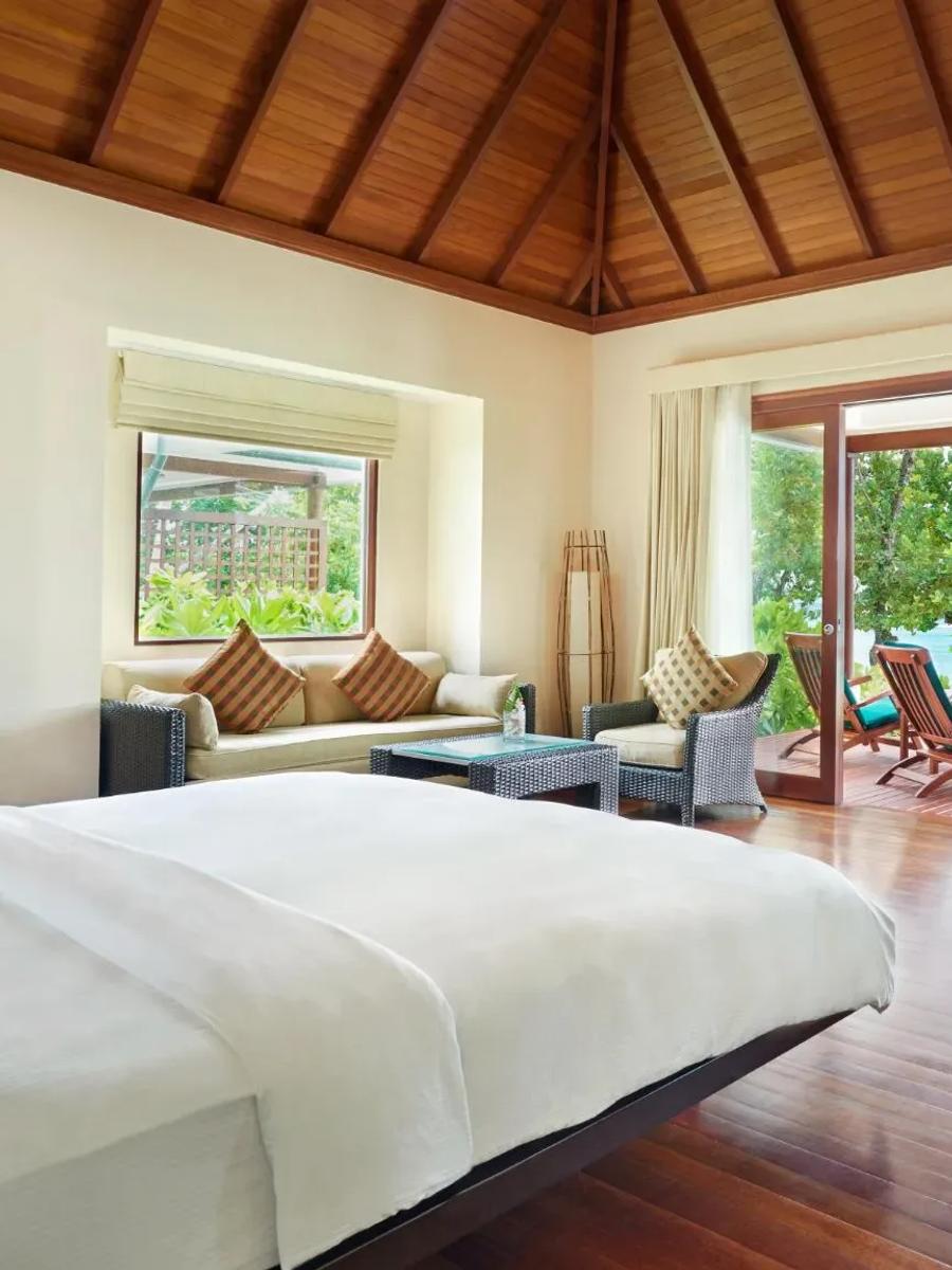 Beach Villa bedroom with a king bed facing a private deck and daybeds, the lagoon visible through the open doors