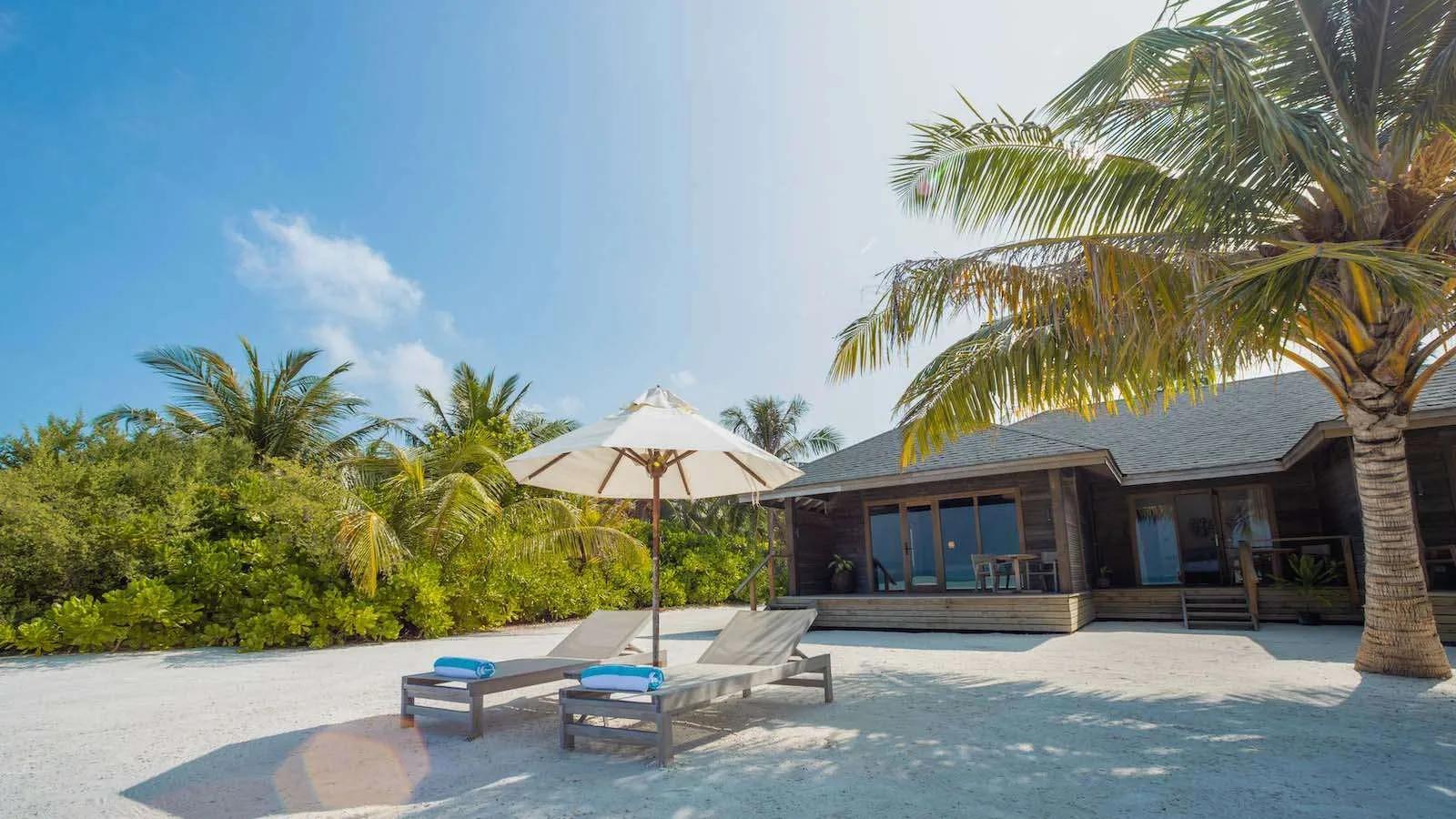 A single-storey Beach Villa exterior at Jawakara, sun loungers and umbrellas on the sand facing the lagoon