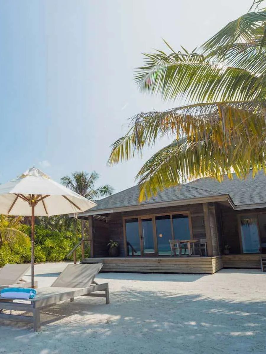A single-storey Beach Villa exterior at Jawakara, sun loungers and umbrellas on the sand facing the lagoon