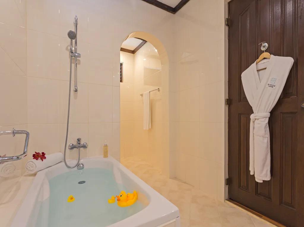 A bathtub with rubber ducks floating in it inside a Deluxe Beachfront Room's bathroom, a robe hanging on the door