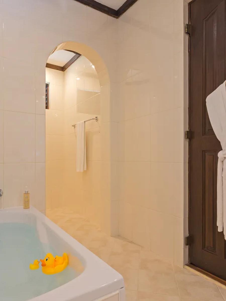A bathtub with rubber ducks floating in it inside a Deluxe Beachfront Room's bathroom, a robe hanging on the door