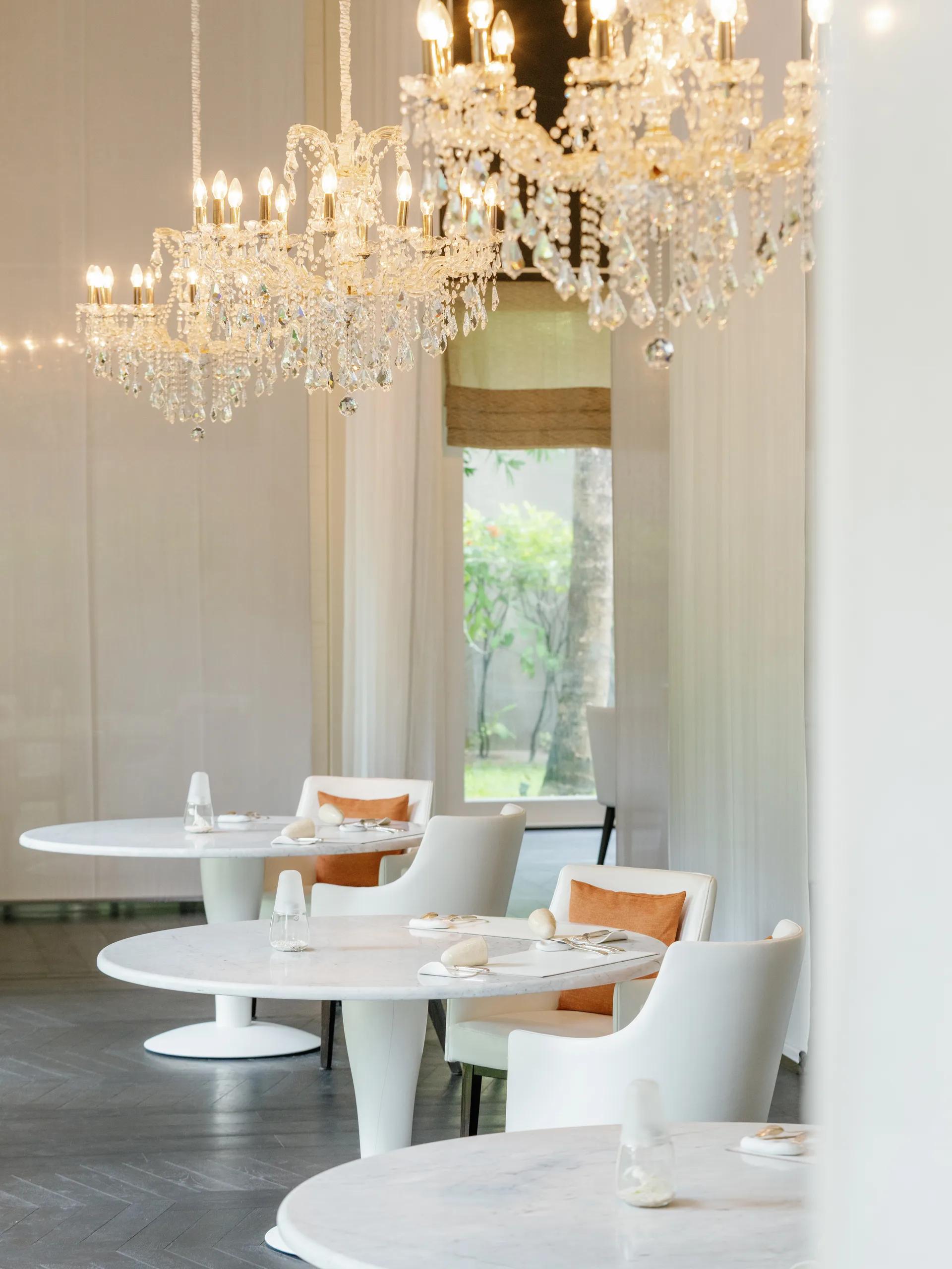 Le 1947's dining room, three crystal chandeliers hanging above a long table set for dinner