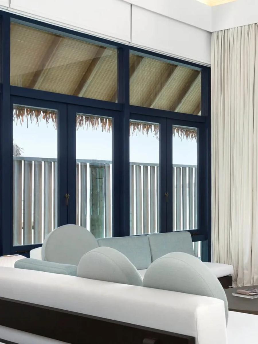 The living area of a Loft Water Villa, glass doors open onto a private overwater deck and the lagoon beyond