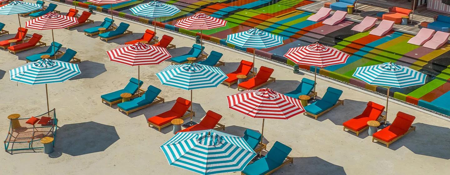 Aerial view of Lazuli Beach Club's striped umbrellas, red and teal loungers and colour-blocked pool deck at SO/ Maldives