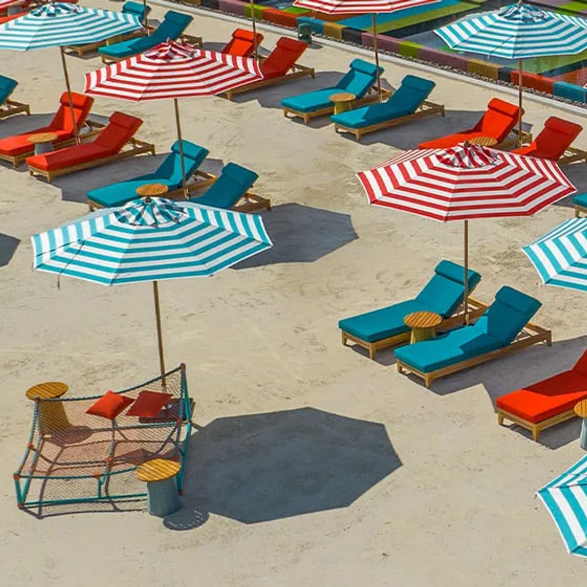 Aerial view of Lazuli Beach Club's striped umbrellas, red and teal loungers and colour-blocked pool deck at SO/ Maldives