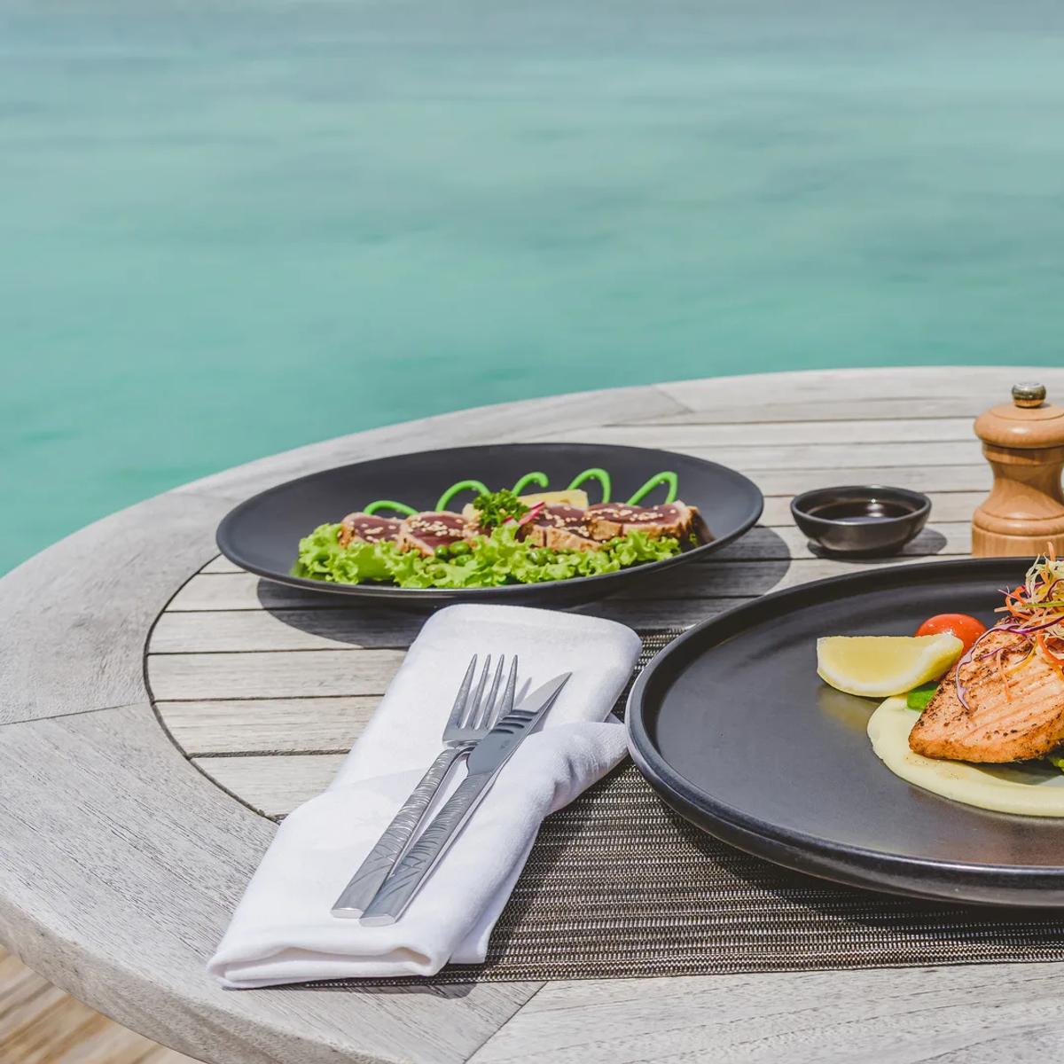 A grilled salmon fillet plated with asparagus and a glass of white wine, the turquoise lagoon in the background at the Grill Bar