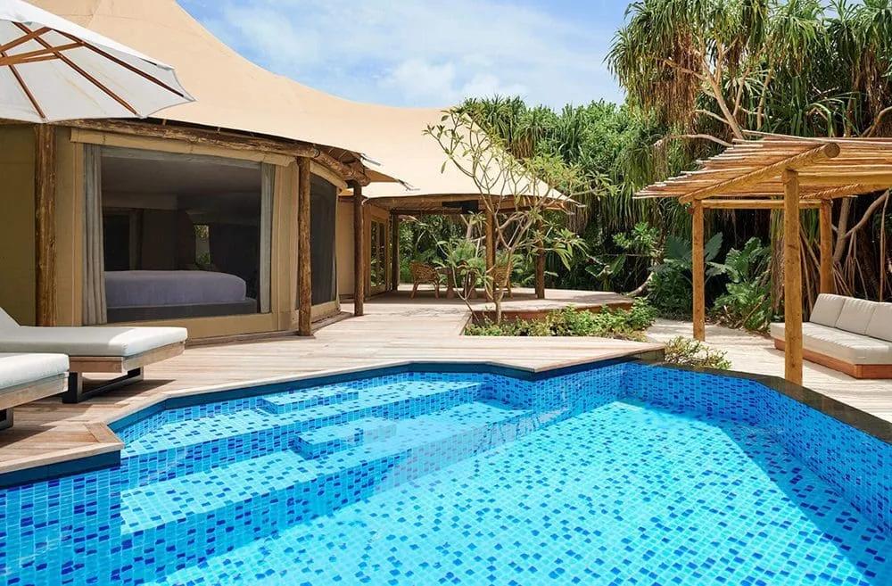 A tented villa's private plunge pool and canvas-roofed pavilion, set on a jungle beach among palms