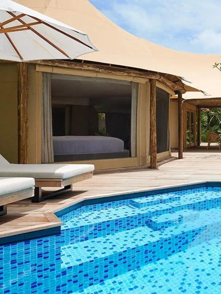 A tented villa's private plunge pool and canvas-roofed pavilion, set on a jungle beach among palms