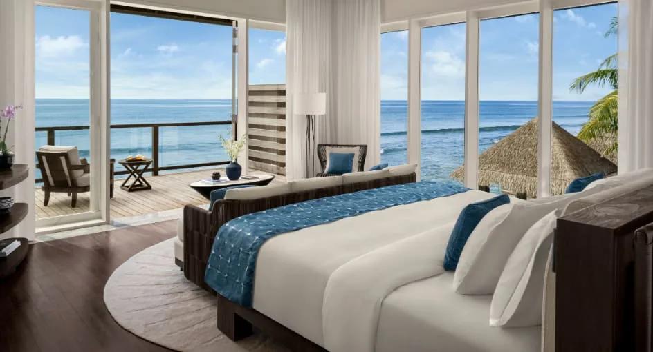 A bedroom with floor-to-ceiling glass doors opening to a private terrace with a hanging daybed and open ocean view