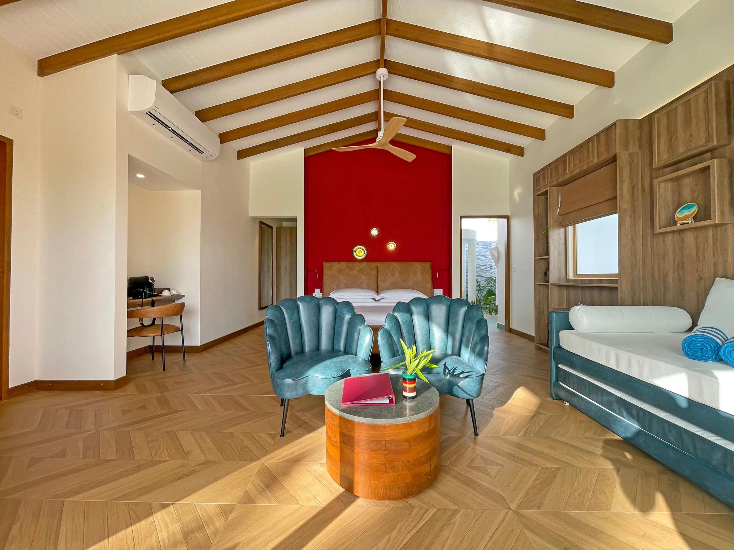A Beach Suite's living area, red accent wall and teal shell-shaped chairs around a low table, a daybed to one side