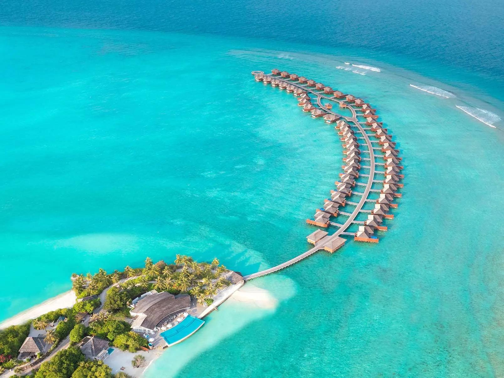 Aerial view of Hideaway Beach Resort & Spa's bow-shaped overwater villa jetty, curving out to a circular sunset deck in Haa Alifu Atoll