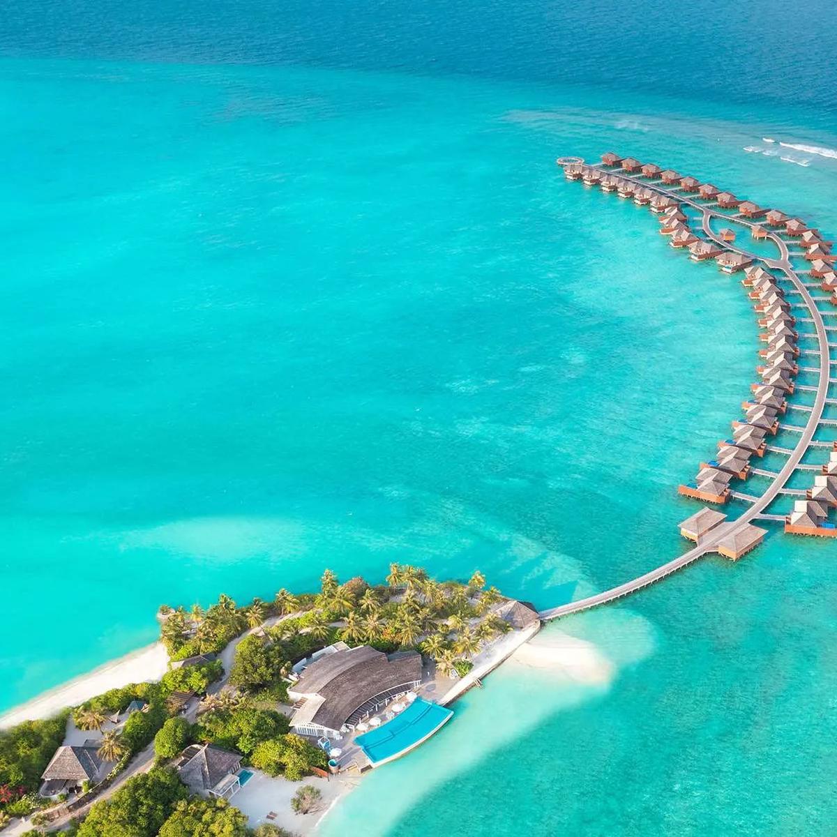 Aerial view of Hideaway Beach Resort & Spa's bow-shaped overwater villa jetty, curving out to a circular sunset deck in Haa Alifu Atoll