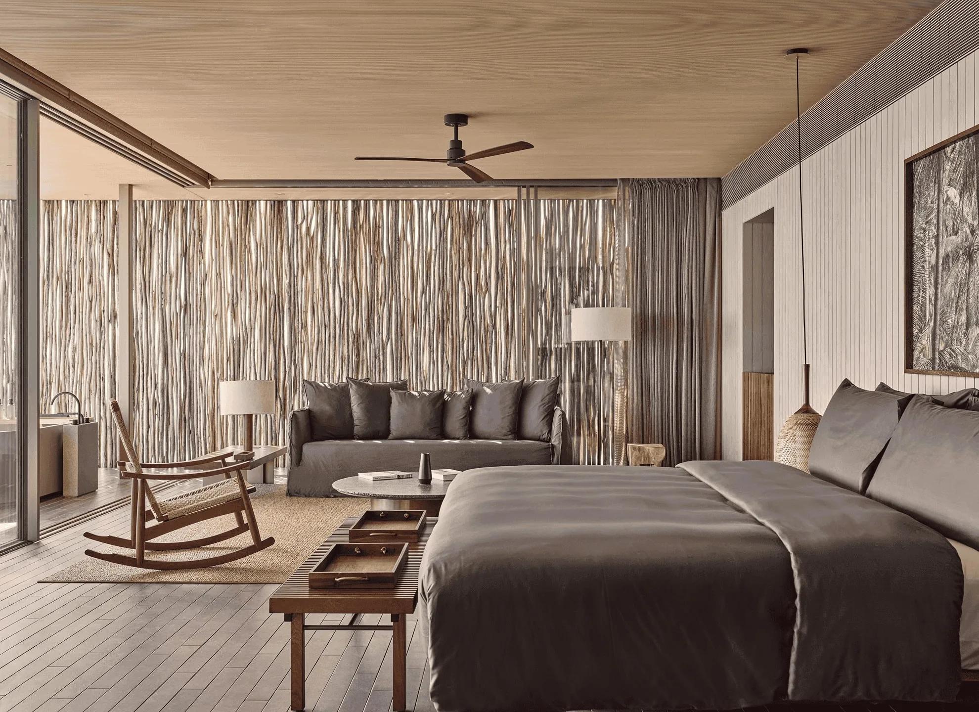 The bedroom and living area at a One-Bedroom Water Pool Villa, a reed-screen wall behind the sofa and a glimpse of the outdoor bath through the glass