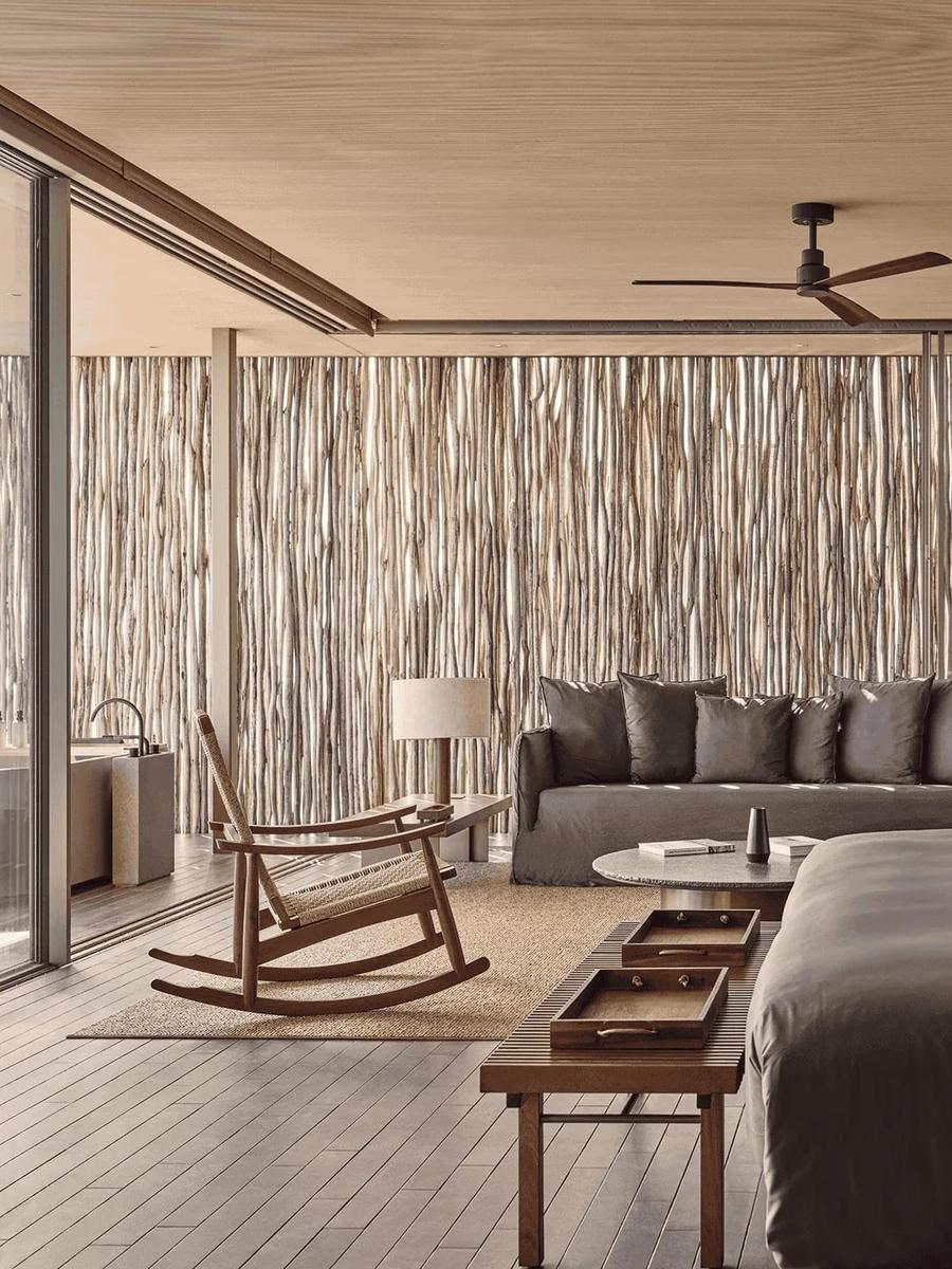 The bedroom and living area at a One-Bedroom Water Pool Villa, a reed-screen wall behind the sofa and a glimpse of the outdoor bath through the glass
