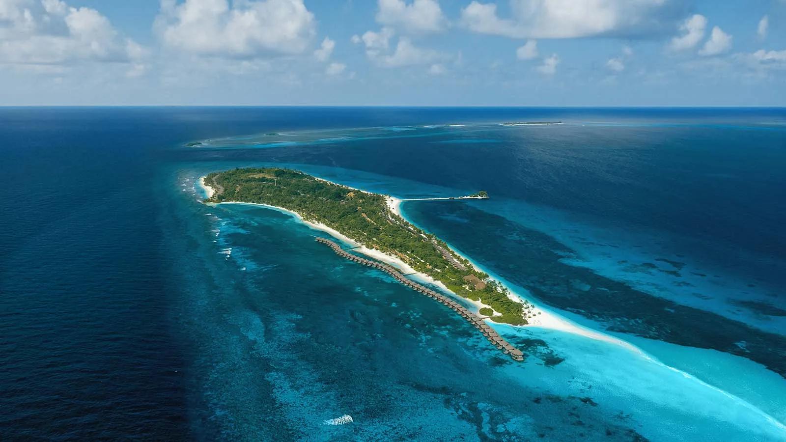 Aerial view of Kuredu's reef-fringed island in Lhaviyani Atoll, overwater villas trailing off its northeast tip