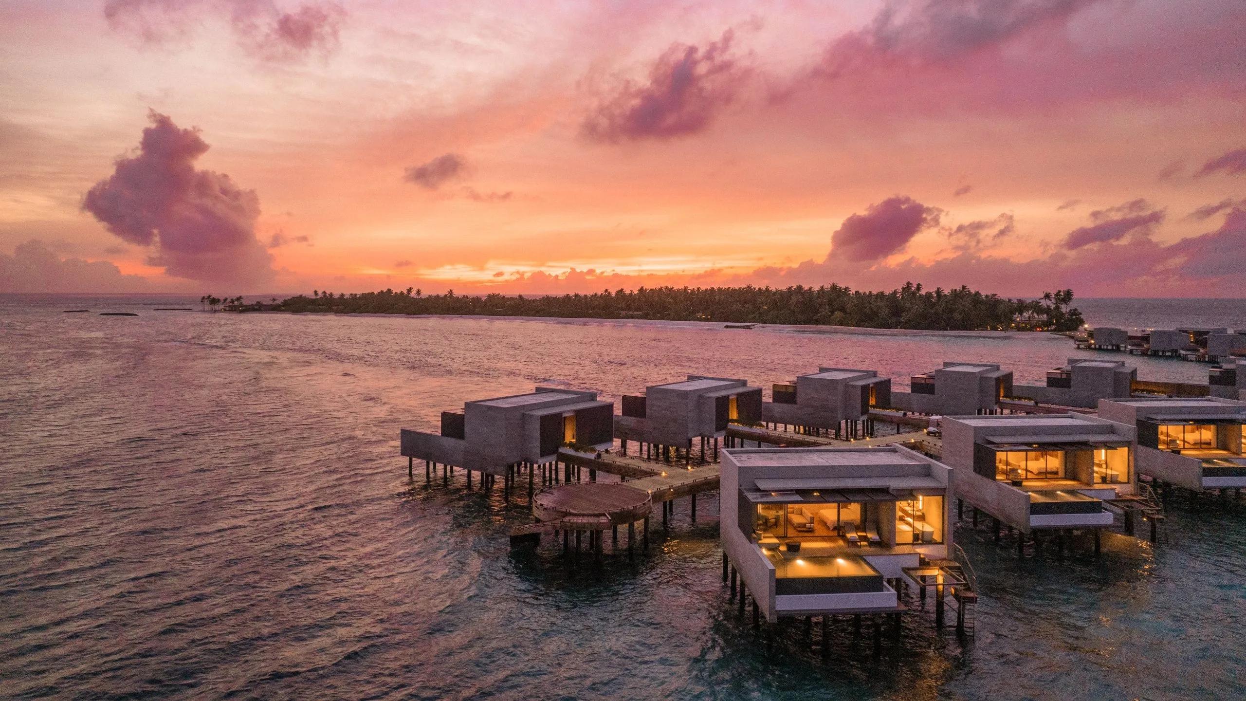 Aerial view at sunset of the overwater villa row stepping out across the lagoon