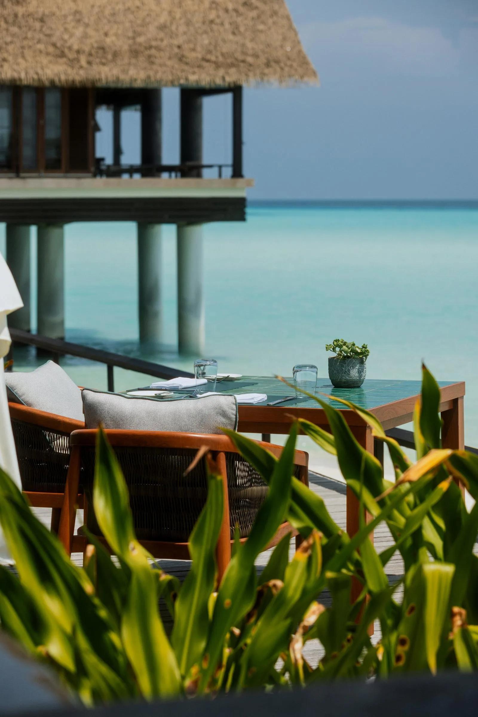 A table set for two on an overwater deck at Rabarbaro, One&Only Reethi Rah's Italian restaurant, with the lagoon and a water villa in view