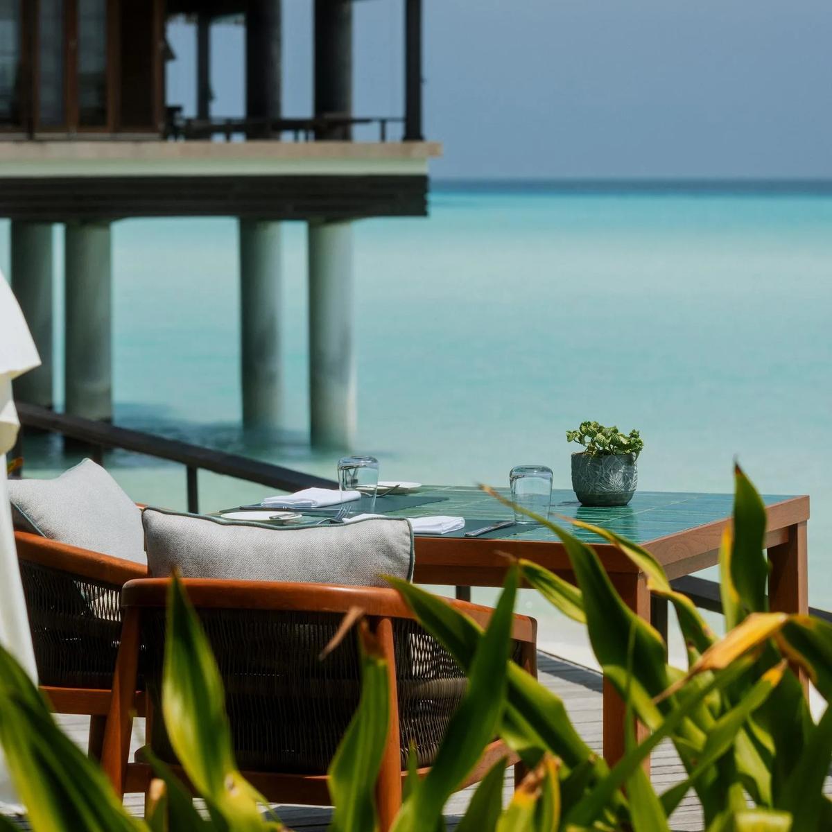 A table set for two on an overwater deck at Rabarbaro, One&Only Reethi Rah's Italian restaurant, with the lagoon and a water villa in view