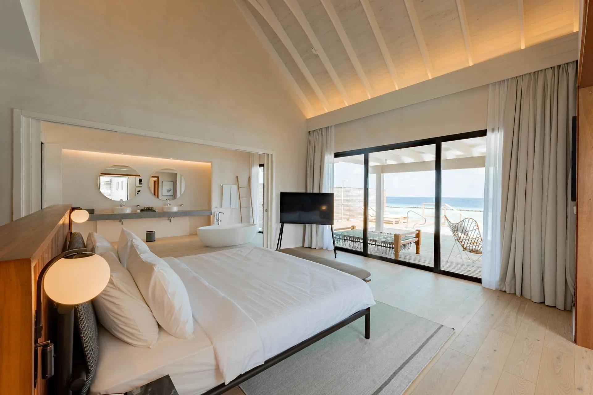 The lagoon-facing bedroom of a Water Pool Villa, glass doors open to the deck