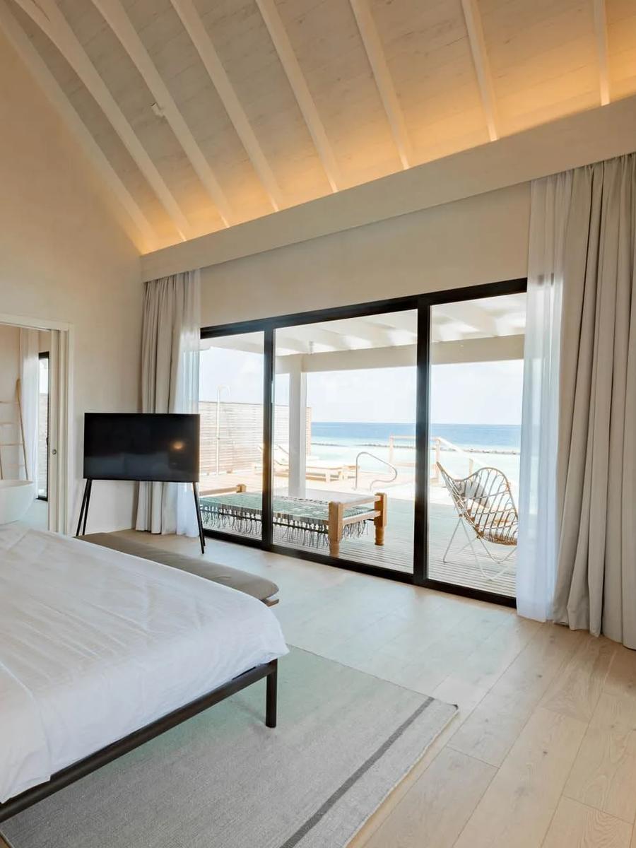 The lagoon-facing bedroom of a Water Pool Villa, glass doors open to the deck