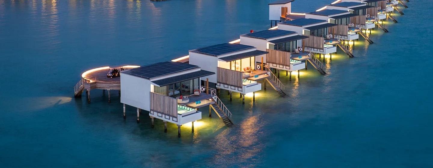 A row of overwater villas at SO/ Maldives lit at dusk, each with its own private pool on the deck