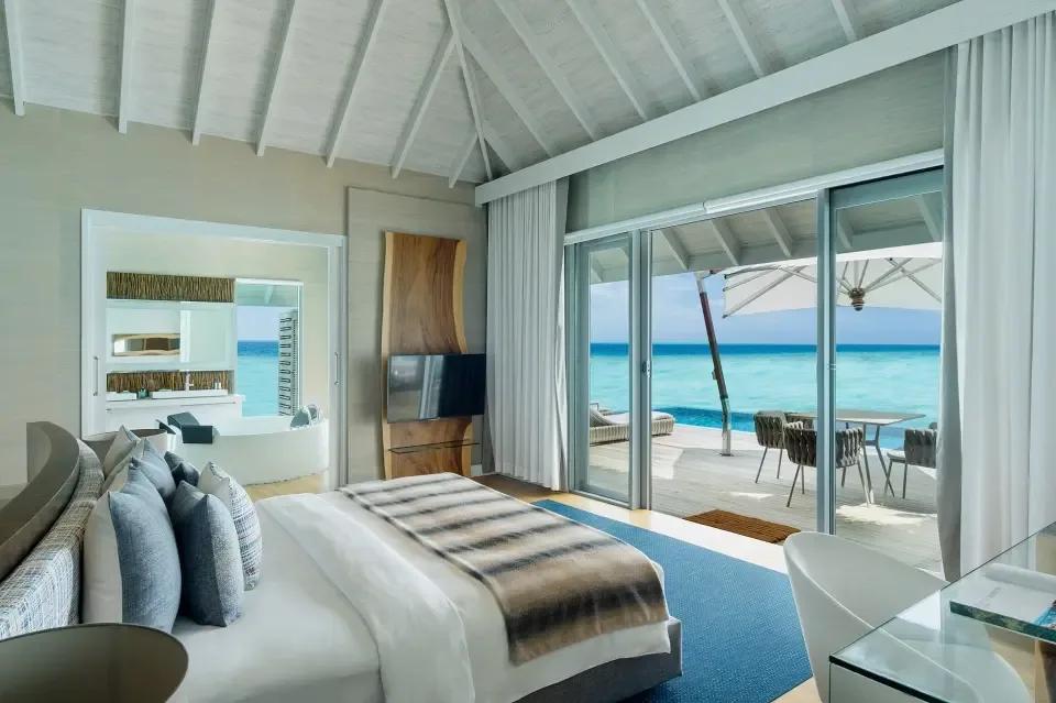 The Water Suite's bedroom opening directly onto its private deck, infinity pool and dining area over the lagoon