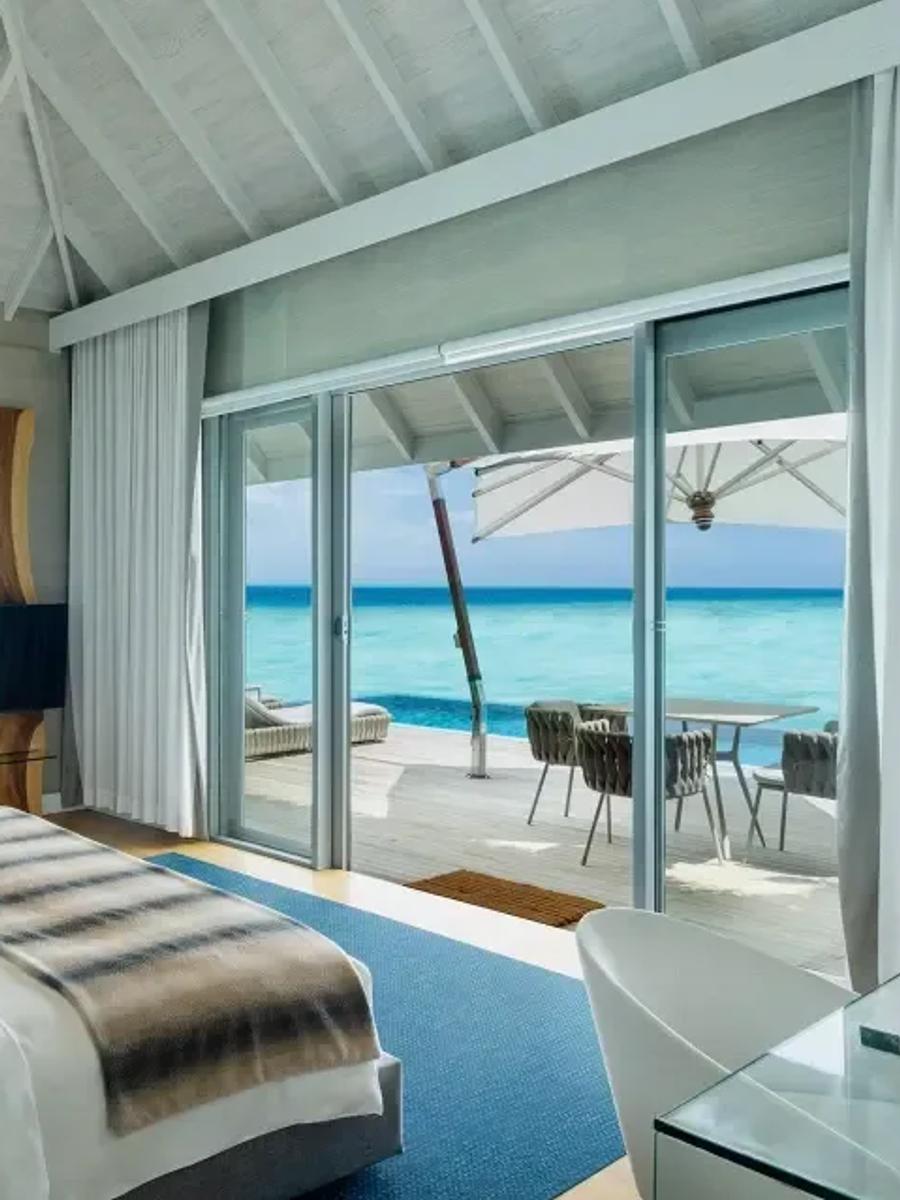 The Water Suite's bedroom opening directly onto its private deck, infinity pool and dining area over the lagoon