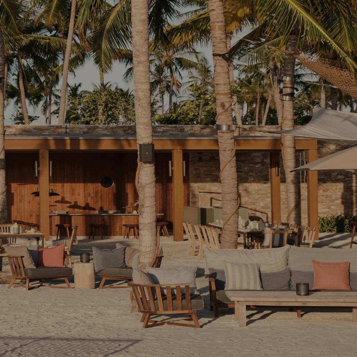 Helios' open-air dining terrace under a canopy of palms, tables and lounge seating set for golden-hour service