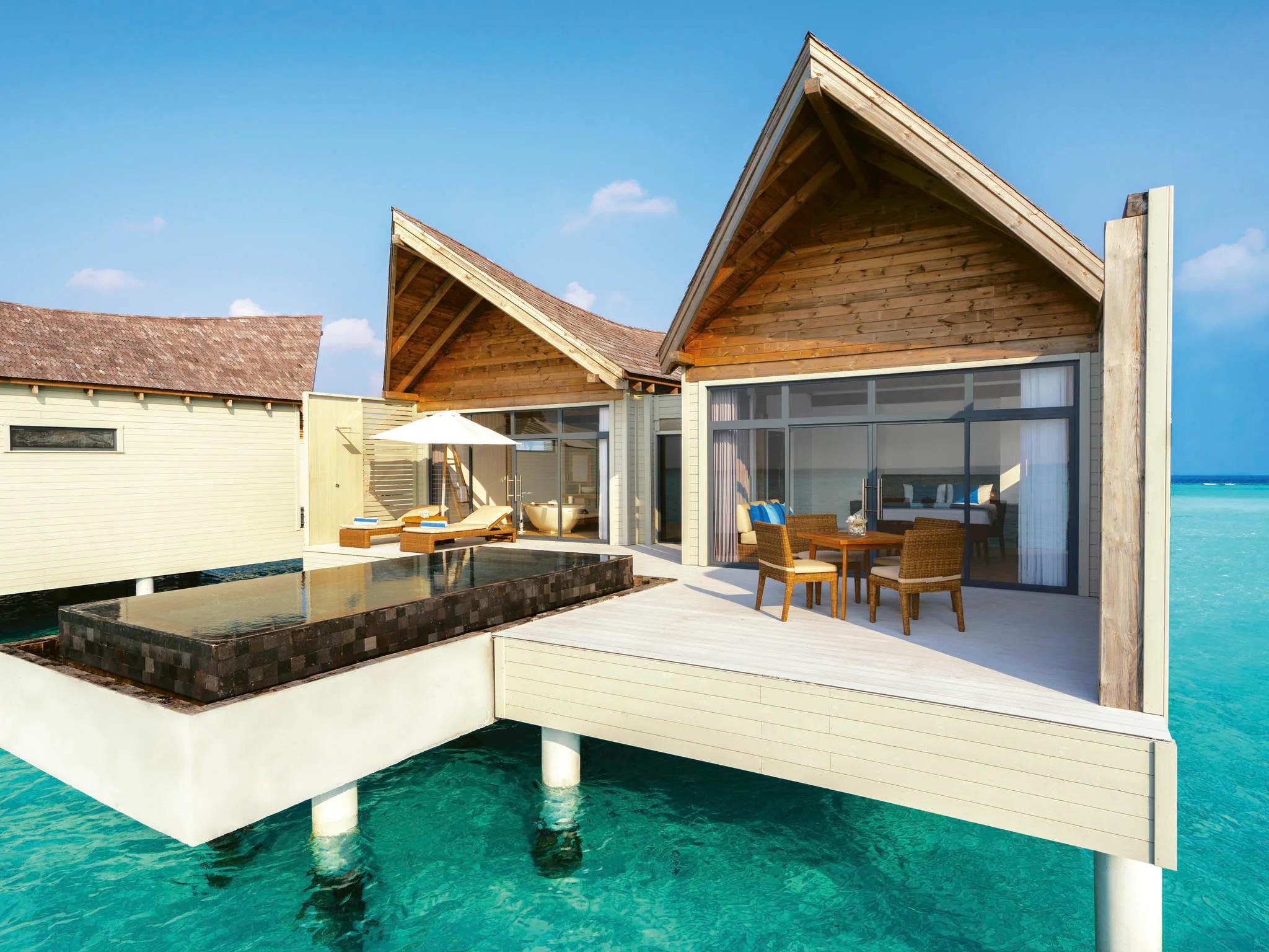 Exterior of an overwater pool villa by day, a private plunge pool and blue-cushioned loungers on the deck, open turquoise lagoon beyond