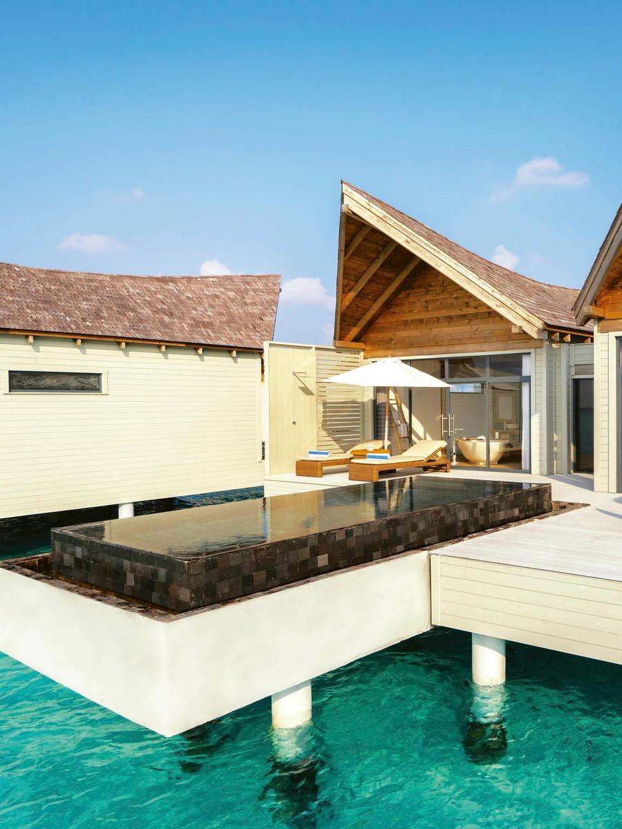 Exterior of an overwater pool villa by day, a private plunge pool and blue-cushioned loungers on the deck, open turquoise lagoon beyond