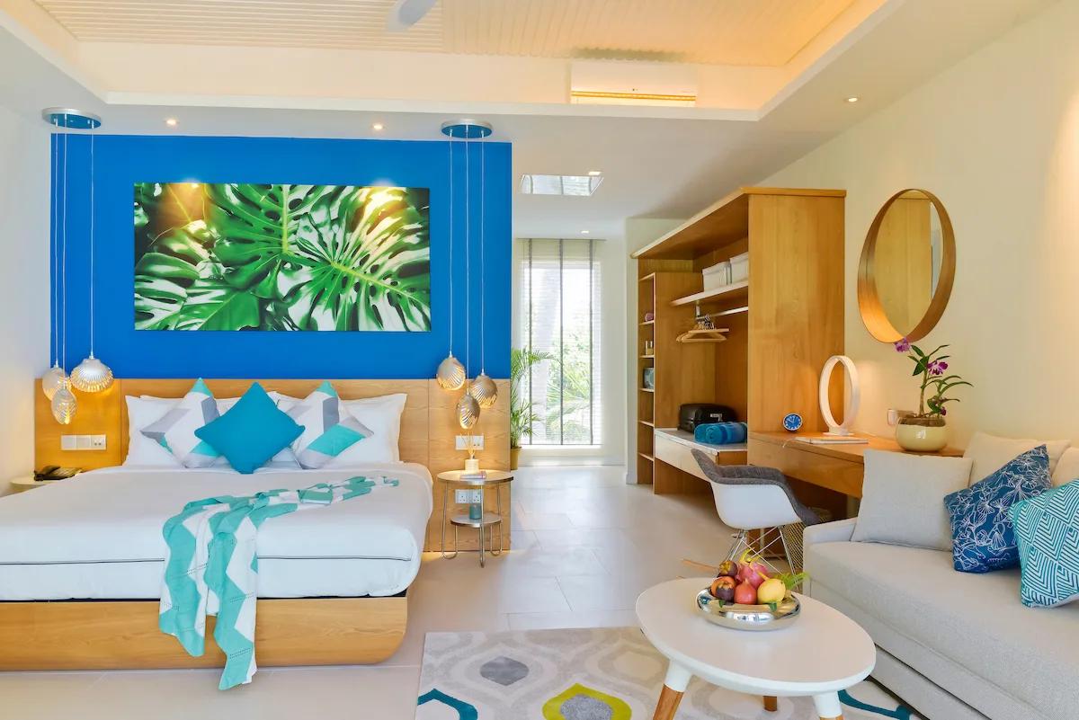 The bedroom of a Beach & Sky Studio, with a blue-walled headboard and a leaf-print artwork