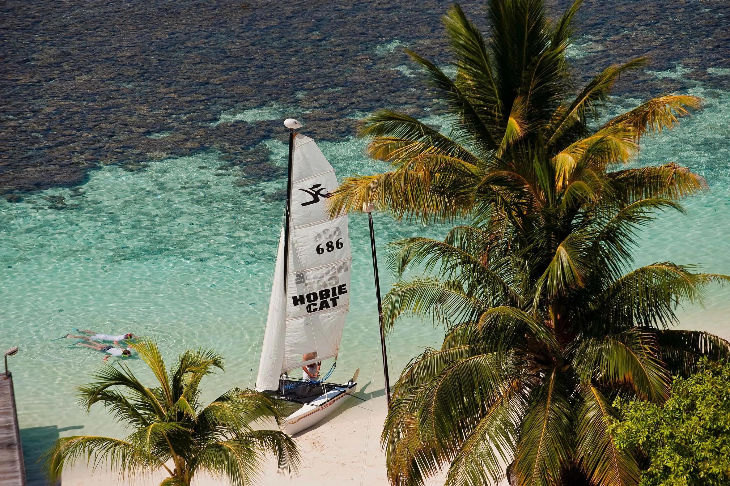 A Hobie Cat sailboat on the beach at Diamonds Athuruga, snorkellers in the shallows nearby