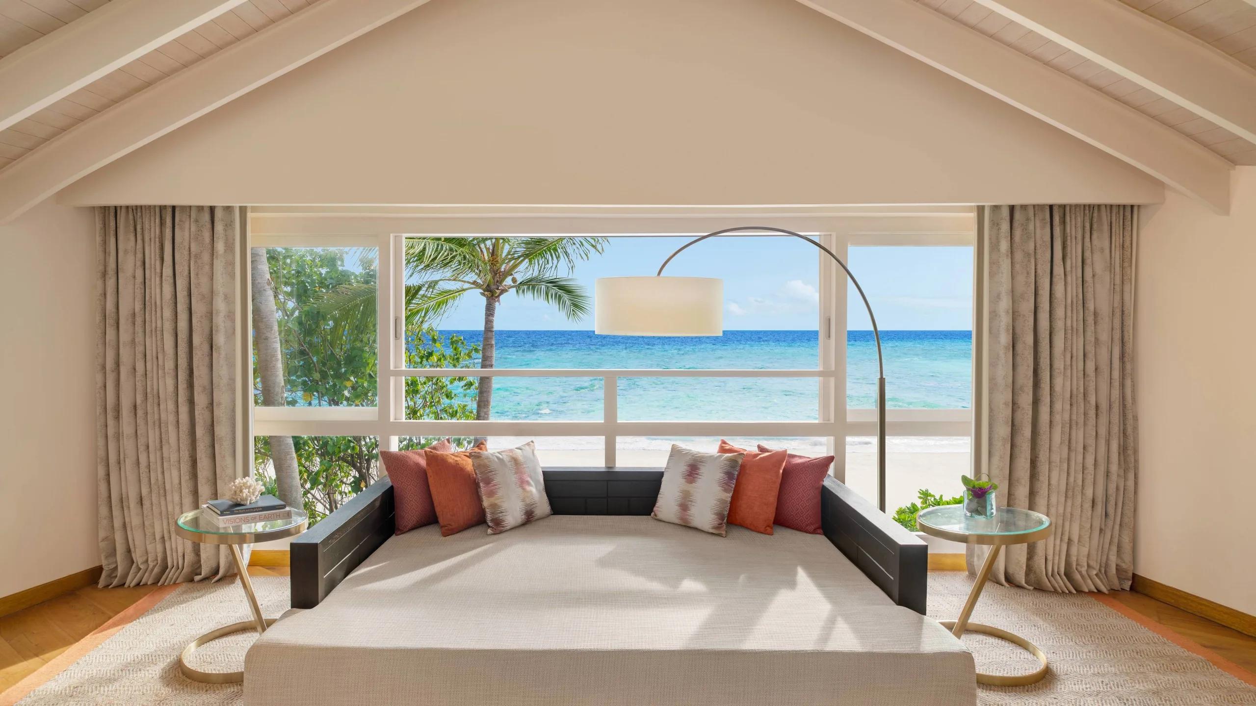 The upstairs lounge of a Duplex Beach Pool Villa, daybed seating looking out past palm trees to the beach