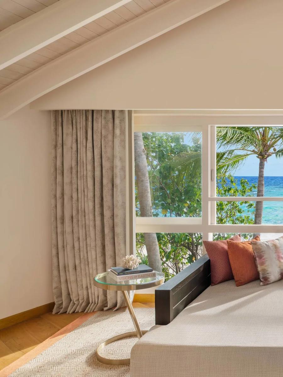 The upstairs lounge of a Duplex Beach Pool Villa, daybed seating looking out past palm trees to the beach