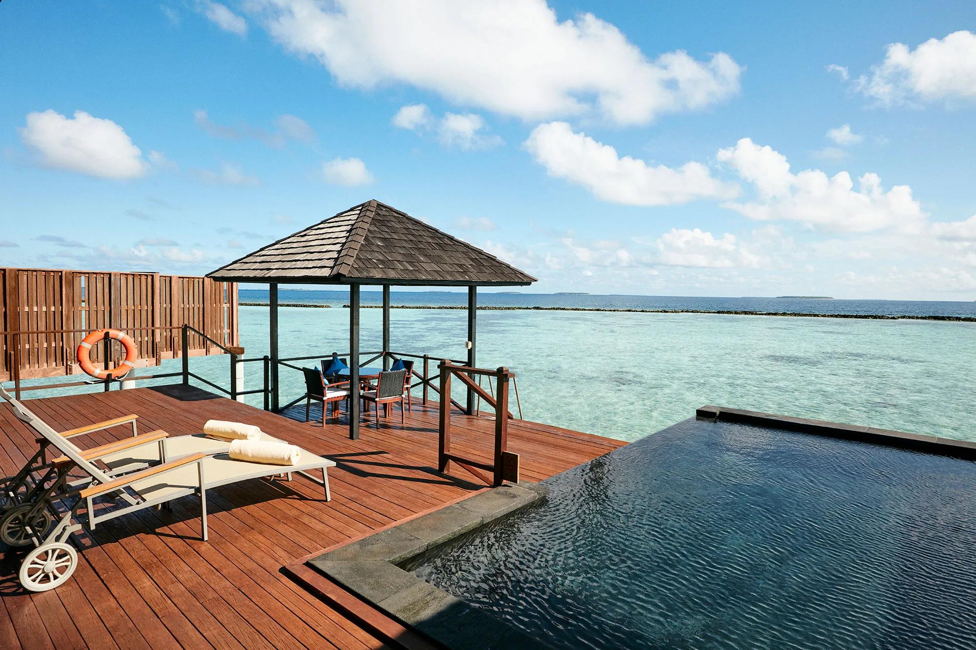 An open-sided pergola dining sala beside the private pool of an Infinity Water Villa, the lagoon beyond