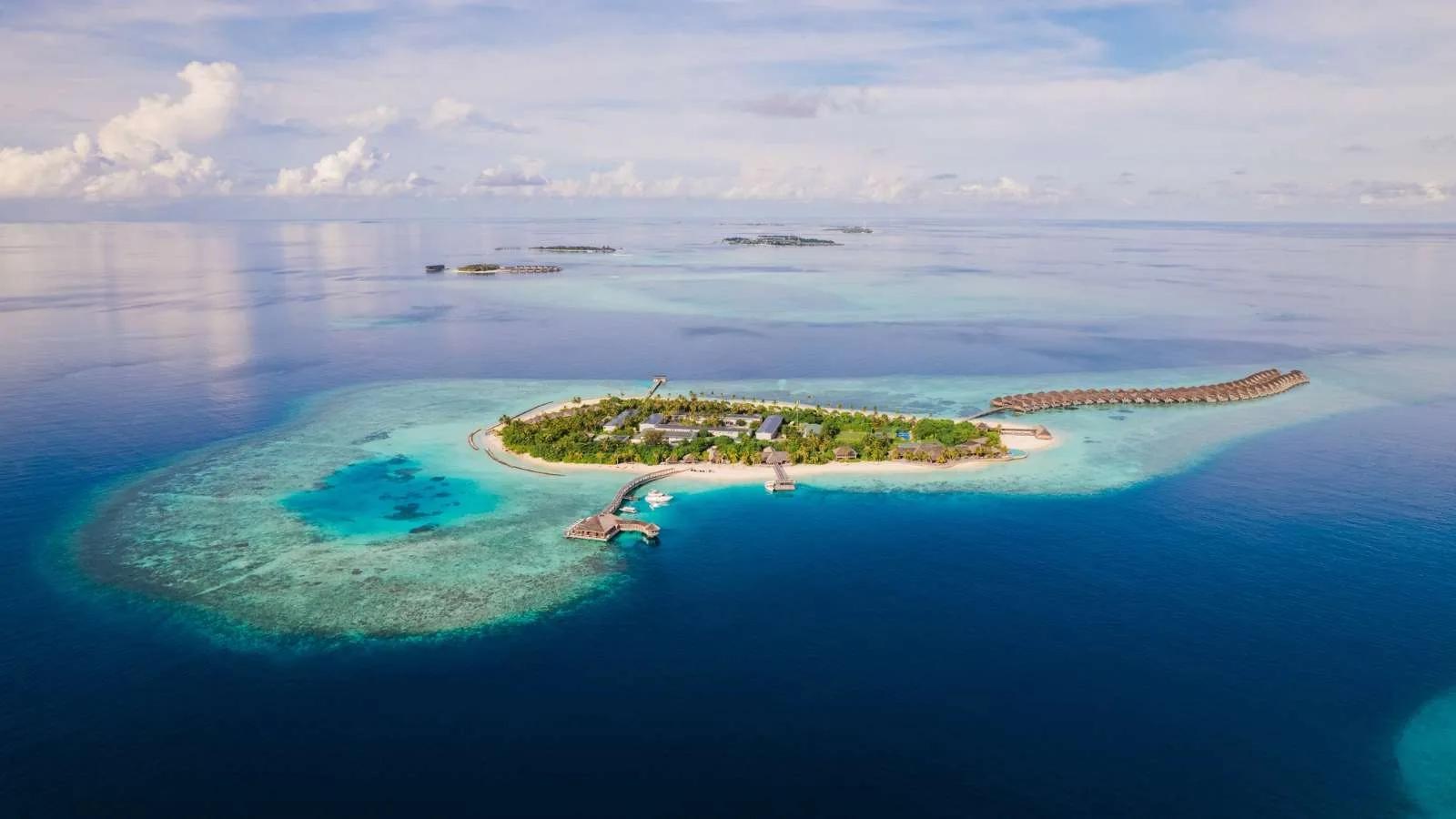 Hurawalhi's single island in Lhaviyani Atoll seen from above, beach villas and jungle interior giving way to a row of overwater villas along the reef edge