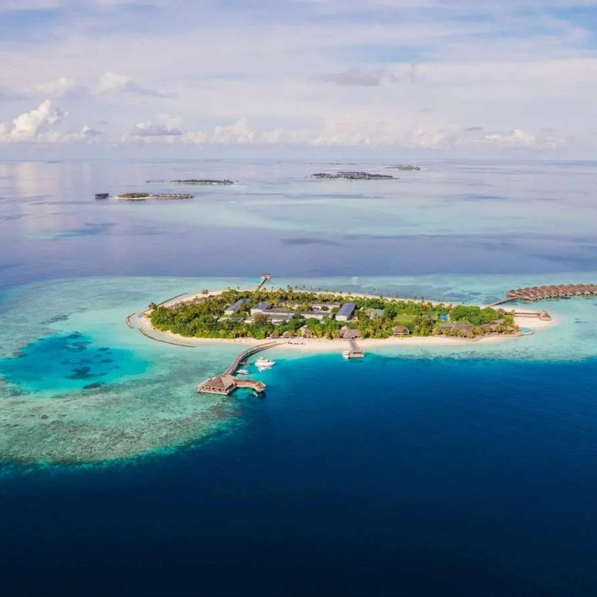 Hurawalhi's single island in Lhaviyani Atoll seen from above, beach villas and jungle interior giving way to a row of overwater villas along the reef edge