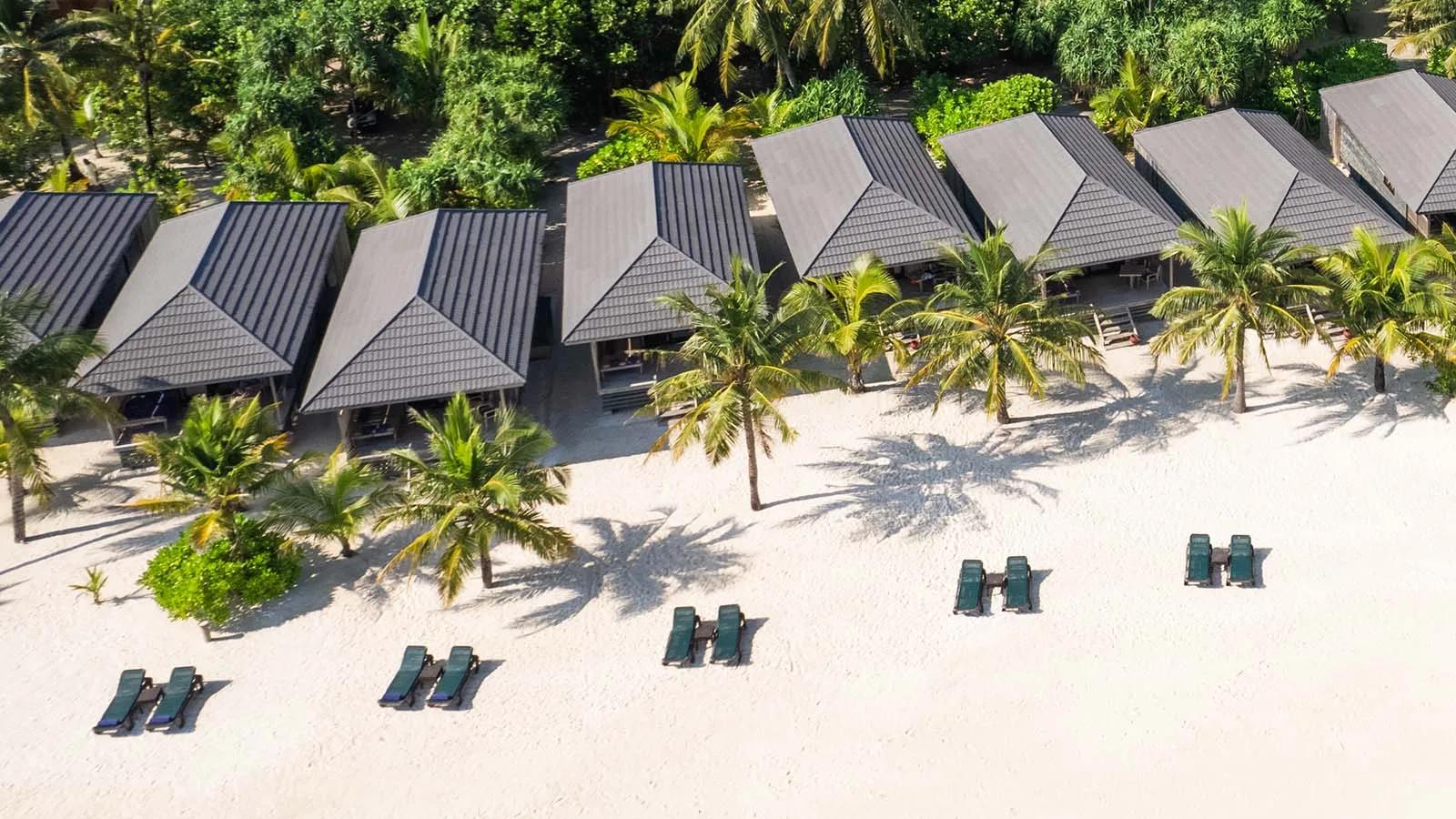 O Beach Villa exterior, a dark wood cottage with a private terrace under palm trees